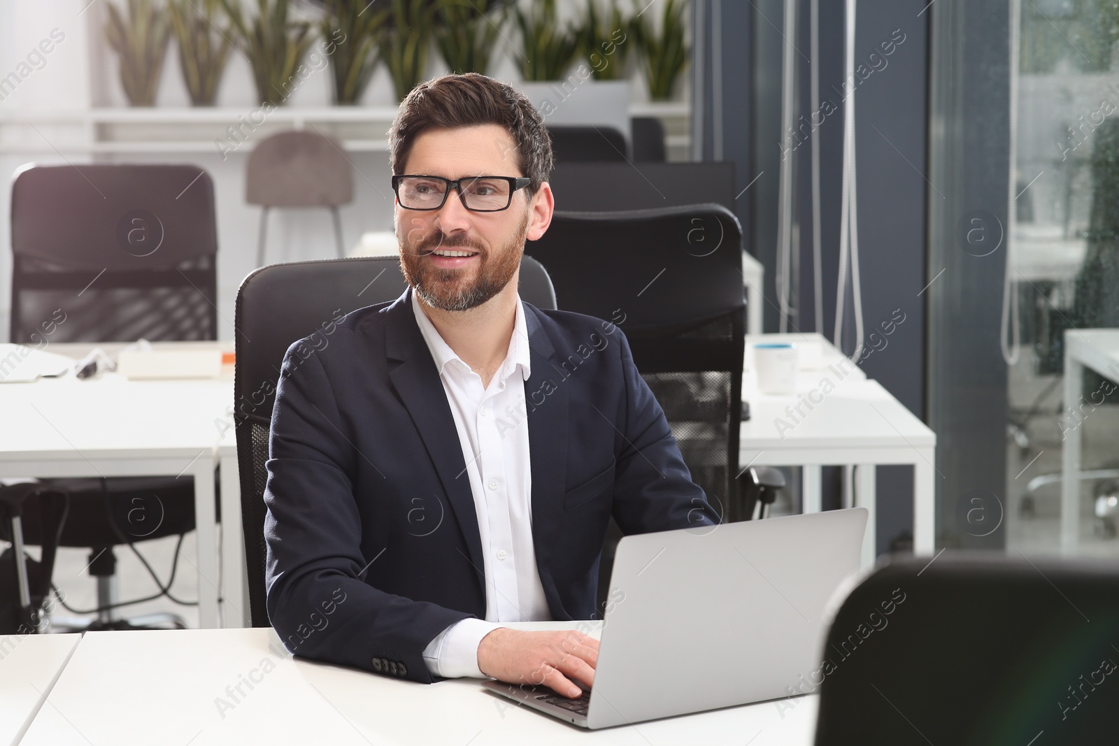 Photo of Man working on laptop at white desk in office