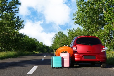 Color suitcases and inflatable ring near family car on highway. Space for text