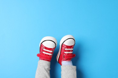 Photo of Little child in stylish red gumshoes on light blue background, top view