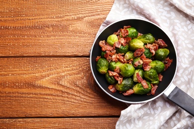 Photo of Tasty roasted Brussels sprouts with bacon on wooden table, top view. Space for text