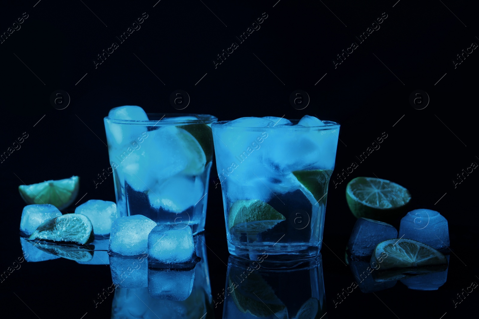 Photo of Shot glasses of vodka with ice cubes and lime slices on dark background