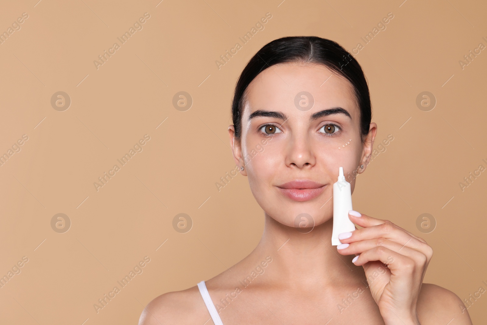 Photo of Beautiful young woman with gel on skin under eye against beige background. Space for text