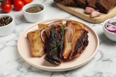 Photo of Tasty fried pork lard with rosemary and onion on white marble table