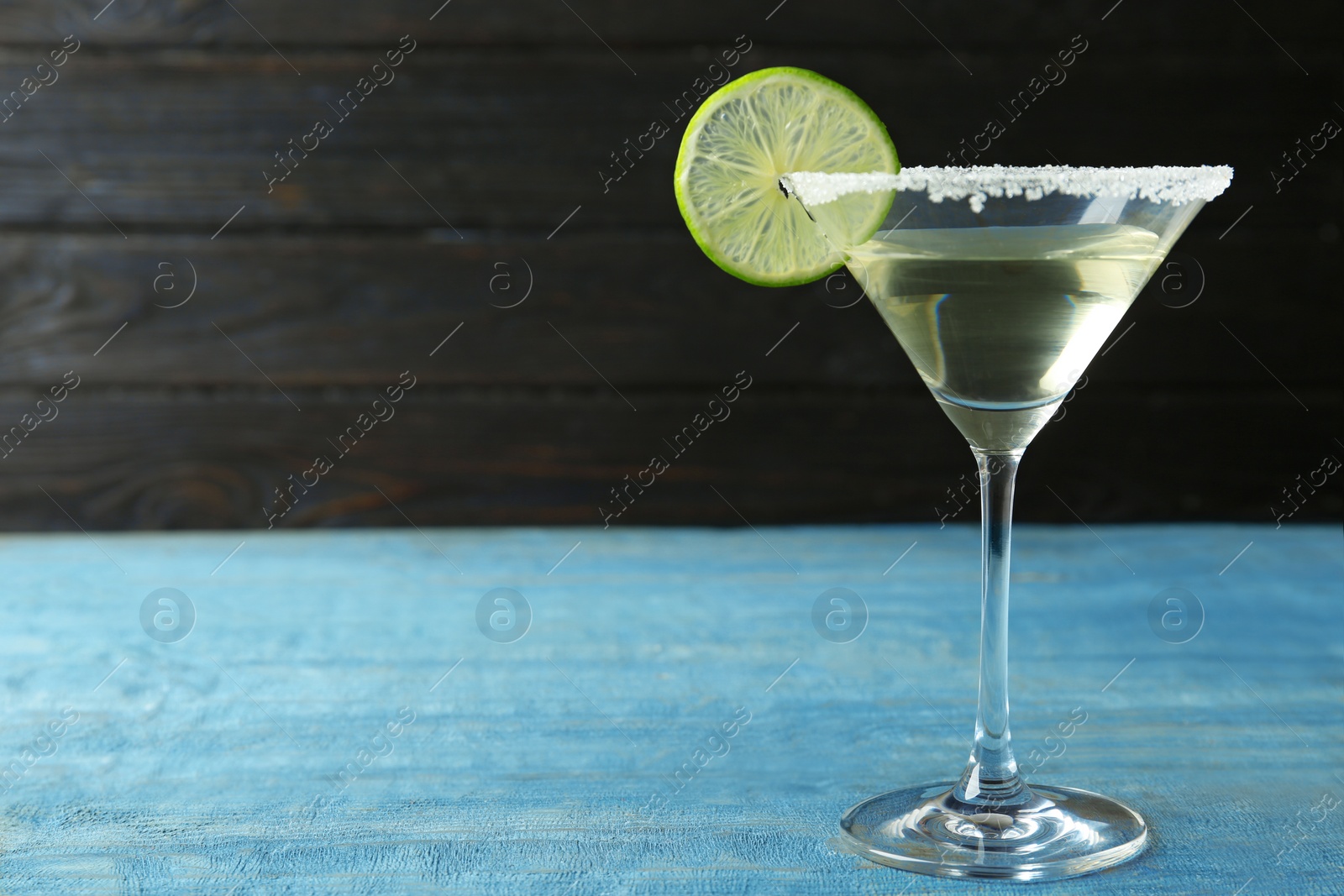 Photo of Glass of Lime Drop Martini cocktail on light blue wooden table. Space for text