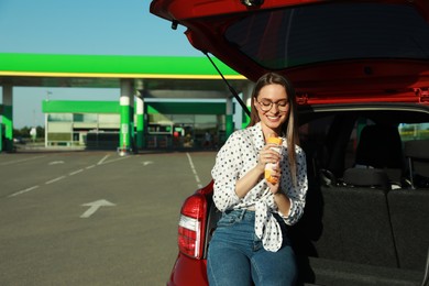 Photo of Beautiful young woman with hot dog near car at gas station