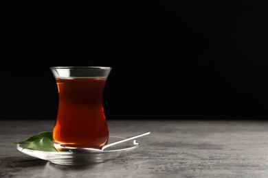 Photo of Glass with traditional Turkish tea on grey table against black background, space for text