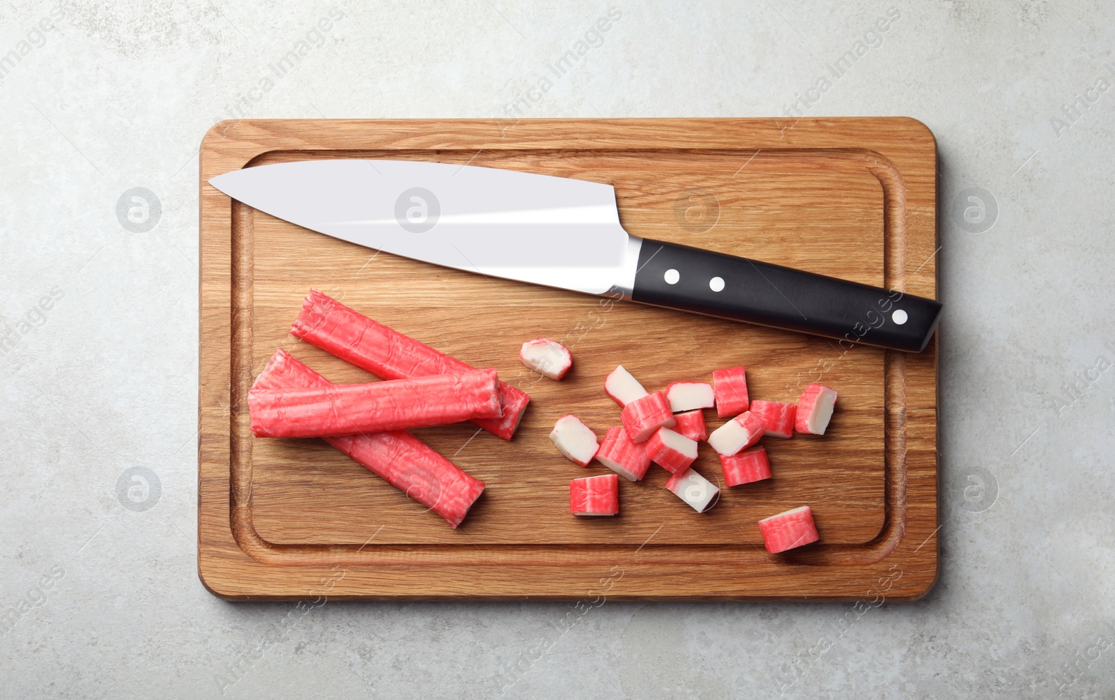 Photo of Board with cut crab sticks and knife on light table, top view