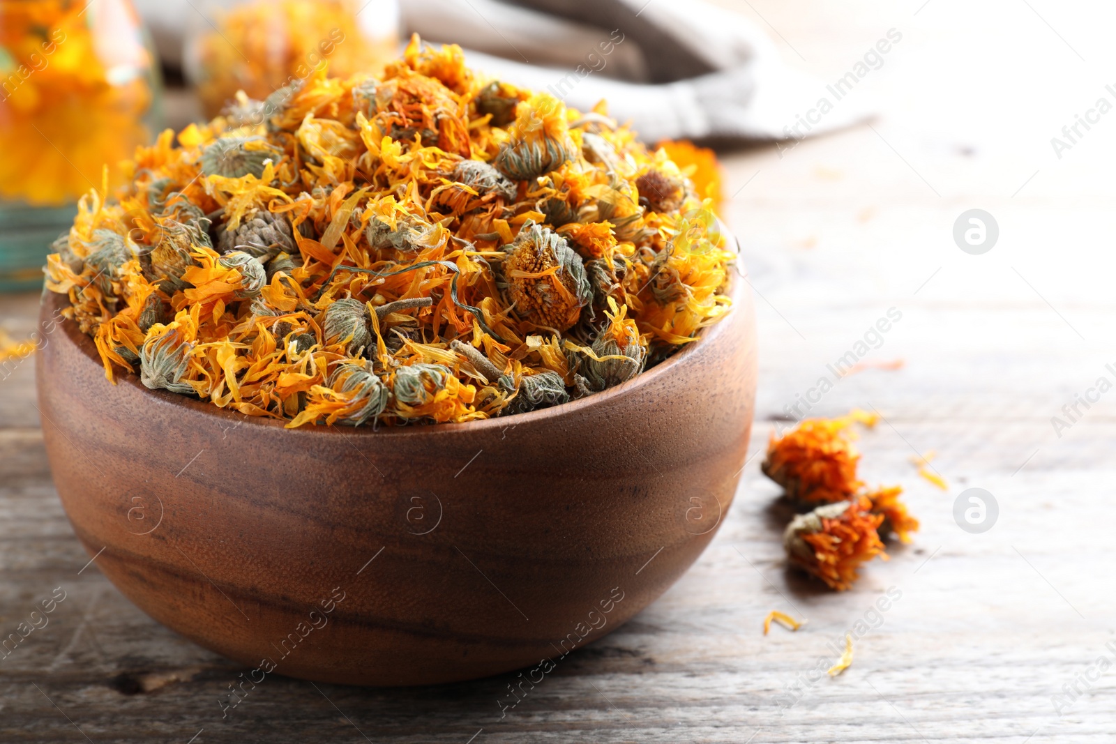 Photo of Bowl of dry calendula flowers on wooden table, closeup