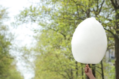 Woman holding sweet cotton candy outdoors, closeup. Space for text