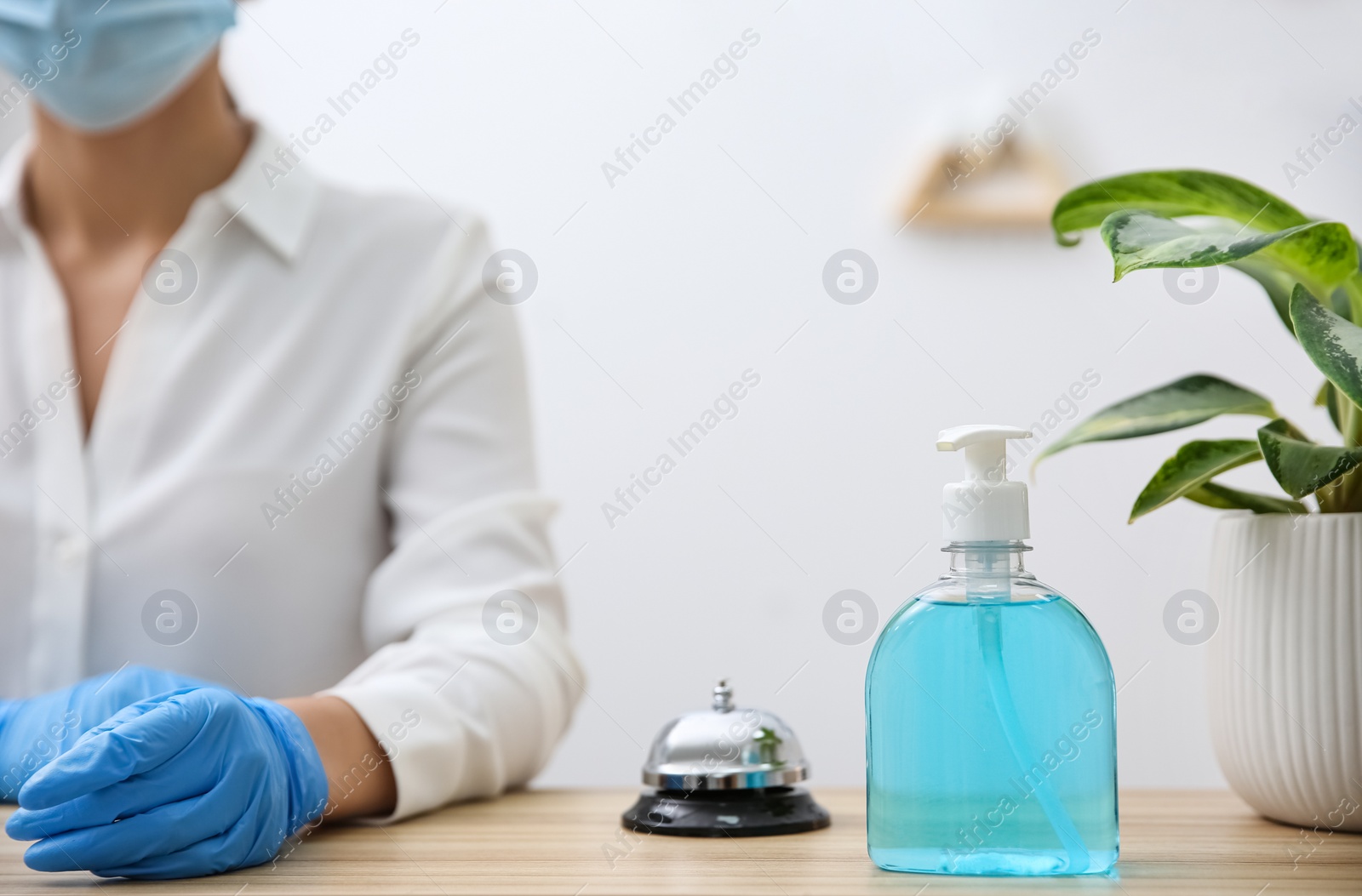 Photo of Receptionist at countertop in hotel, focus on dispenser bottle with antiseptic gel and service bell