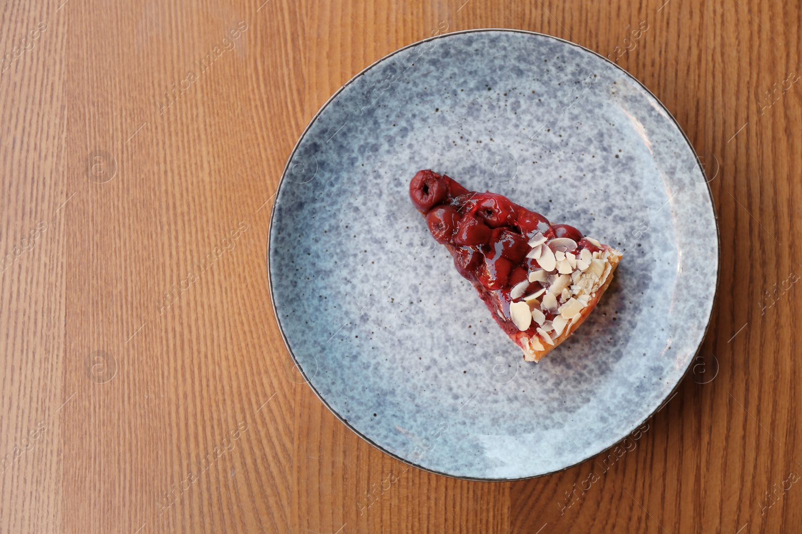 Photo of Plate with slice of cherry cake on wooden table, top view