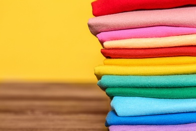 Photo of Stack of colorful t-shirts on table against color background