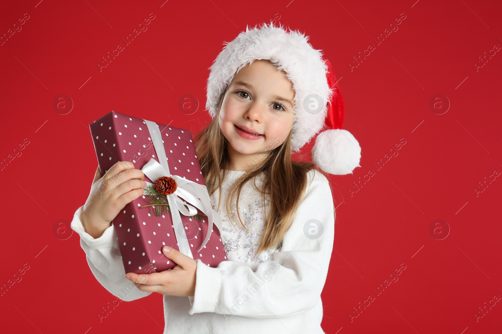 Photo of Cute child in Santa hat with Christmas gift on red background