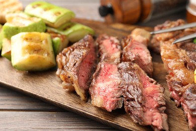 Photo of Delicious grilled beef steak and zucchini on wooden table, closeup