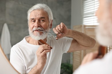 Senior man trimming mustache with scissors near mirror in bathroom