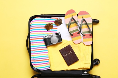 Photo of Open suitcase with beach objects on yellow background, top view