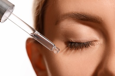 Woman applying cosmetic serum onto her face on white background, closeup