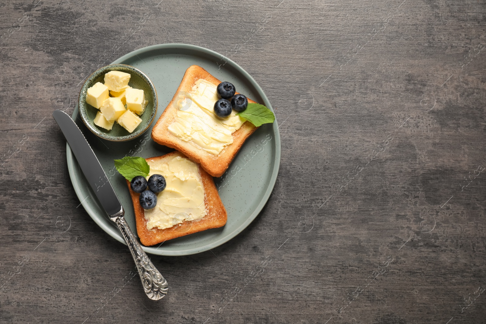 Photo of Delicious toasts served with butter and blueberries on grey wooden table, top view. Space for text