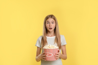 Emotional teenage girl with popcorn during cinema show on color background