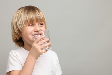 Photo of Happy little boy drinking fresh water on light grey background. Space for text