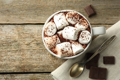 Delicious hot chocolate with marshmallows, cocoa powder and pieces on wooden table, flat lay. Space for text