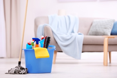 Photo of Bucket with cleaning supplies on floor indoors. Space for text