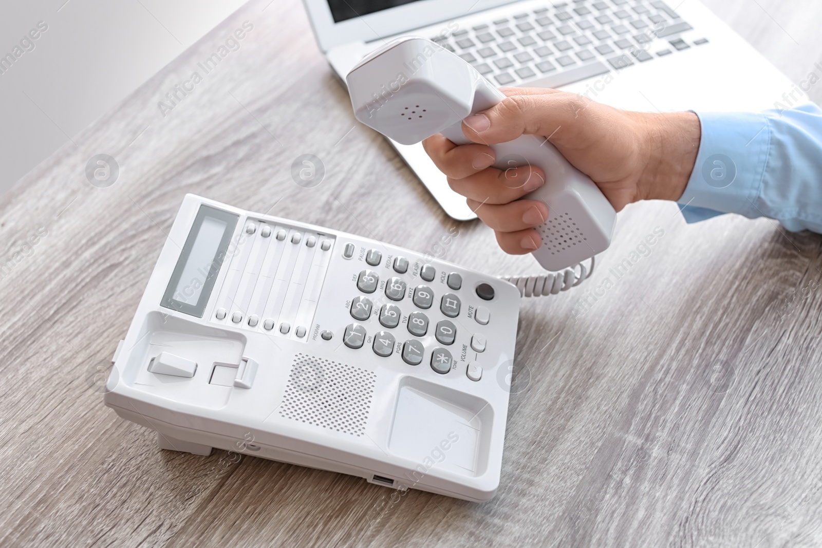 Photo of Man picking up telephone at table in office