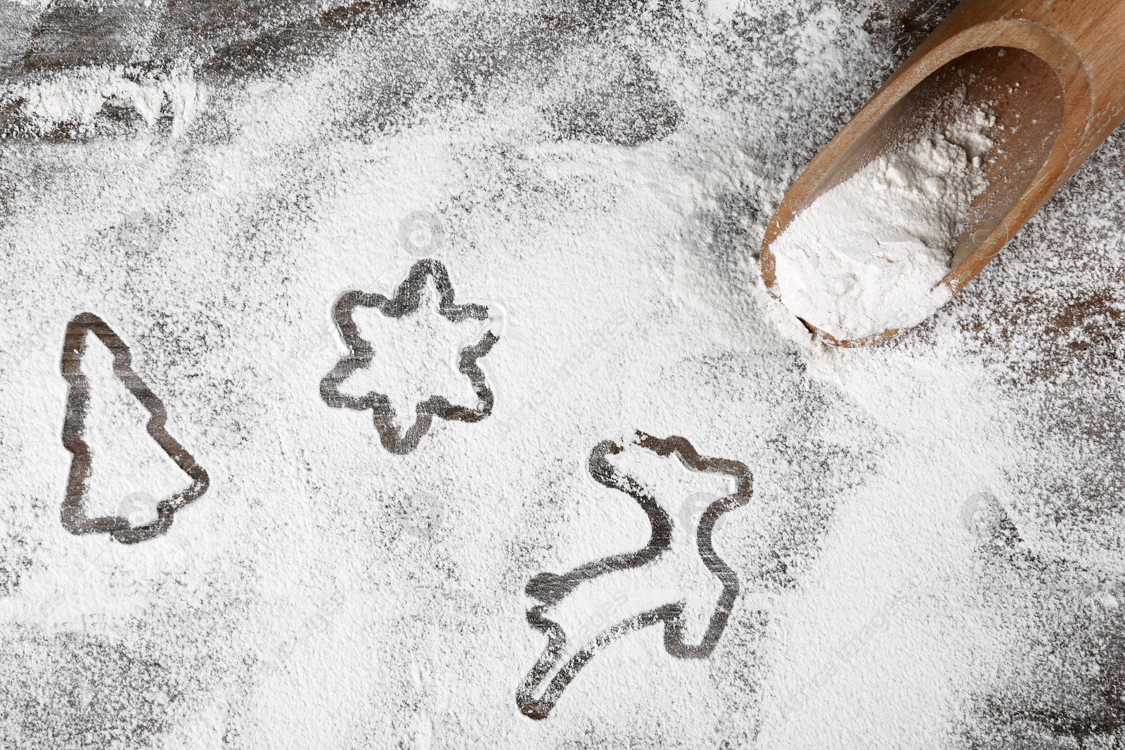 Photo of Different Christmas cookie shapes made of flour near scoop on wooden table, flat lay