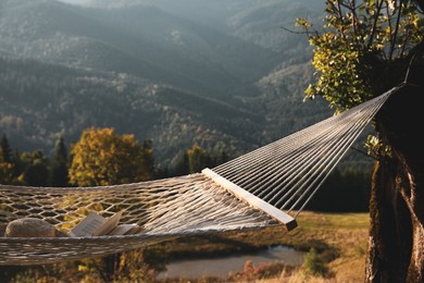 Comfortable net hammock with hat and book in mountains on sunny day