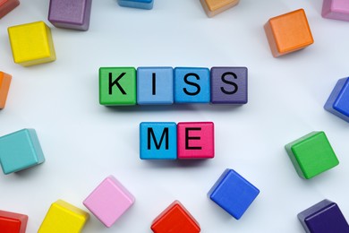 Photo of Colorful cubes with phrase Kiss Me on white background, flat lay