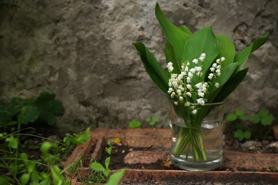 Photo of Beautiful lily of the valley flowers in glass vase on stone parapet outdoors, space for text