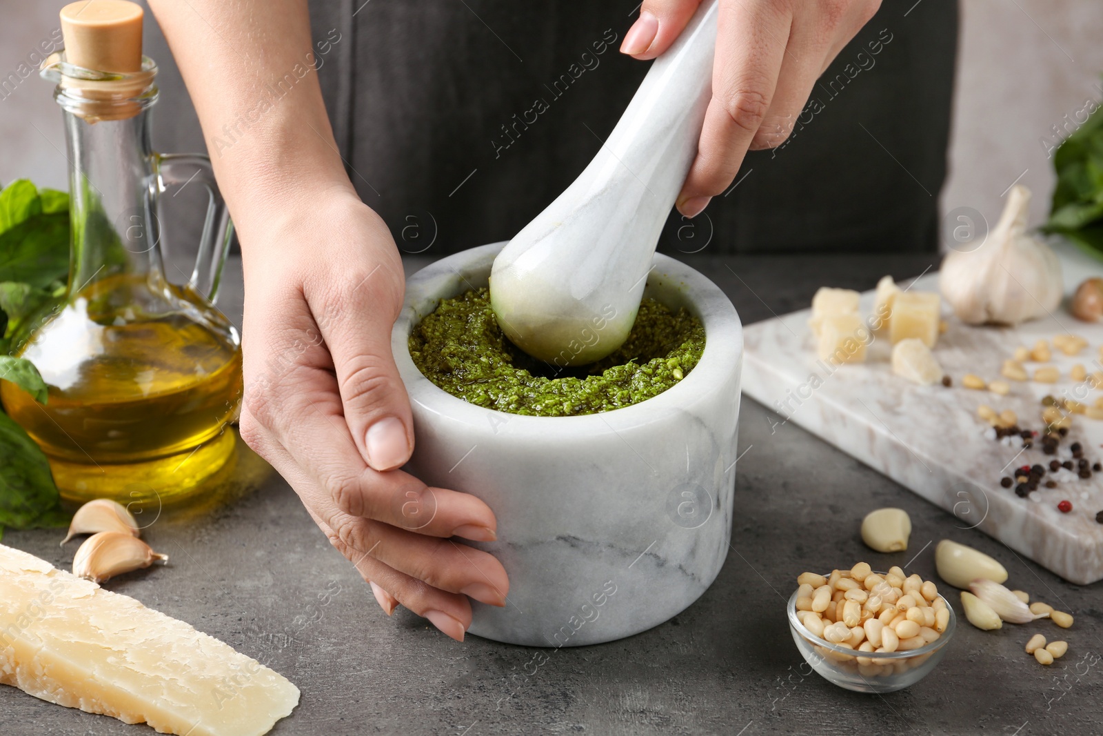 Photo of Woman mashing pesto sauce in mortar at table, closeup