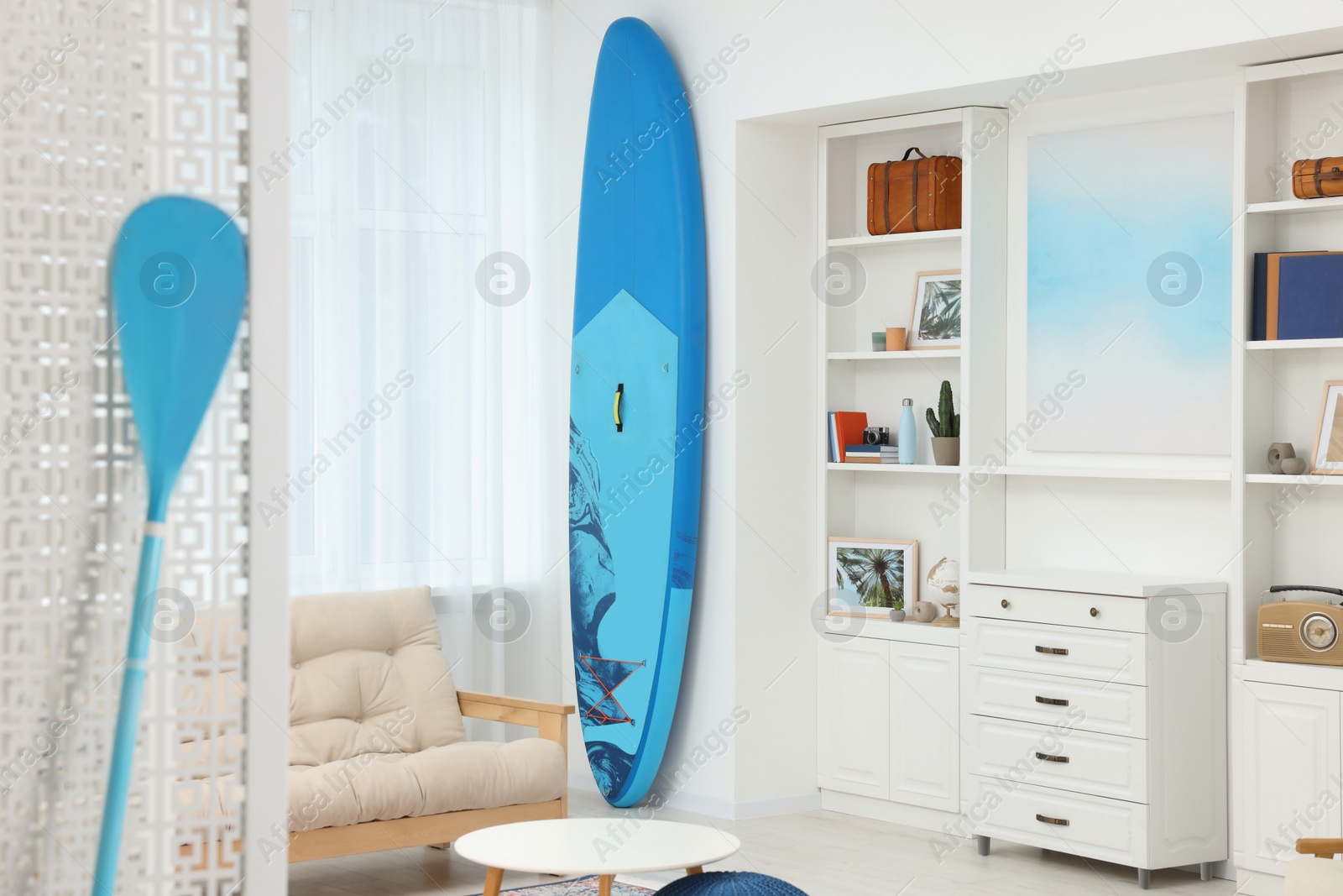 Photo of SUP board and modern furniture in stylish living room. Interior design