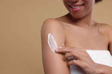 Photo of Young woman applying body cream onto arm on beige background, closeup. Space for text