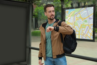 Image of Young man with backpack waiting for public transport at bus stop