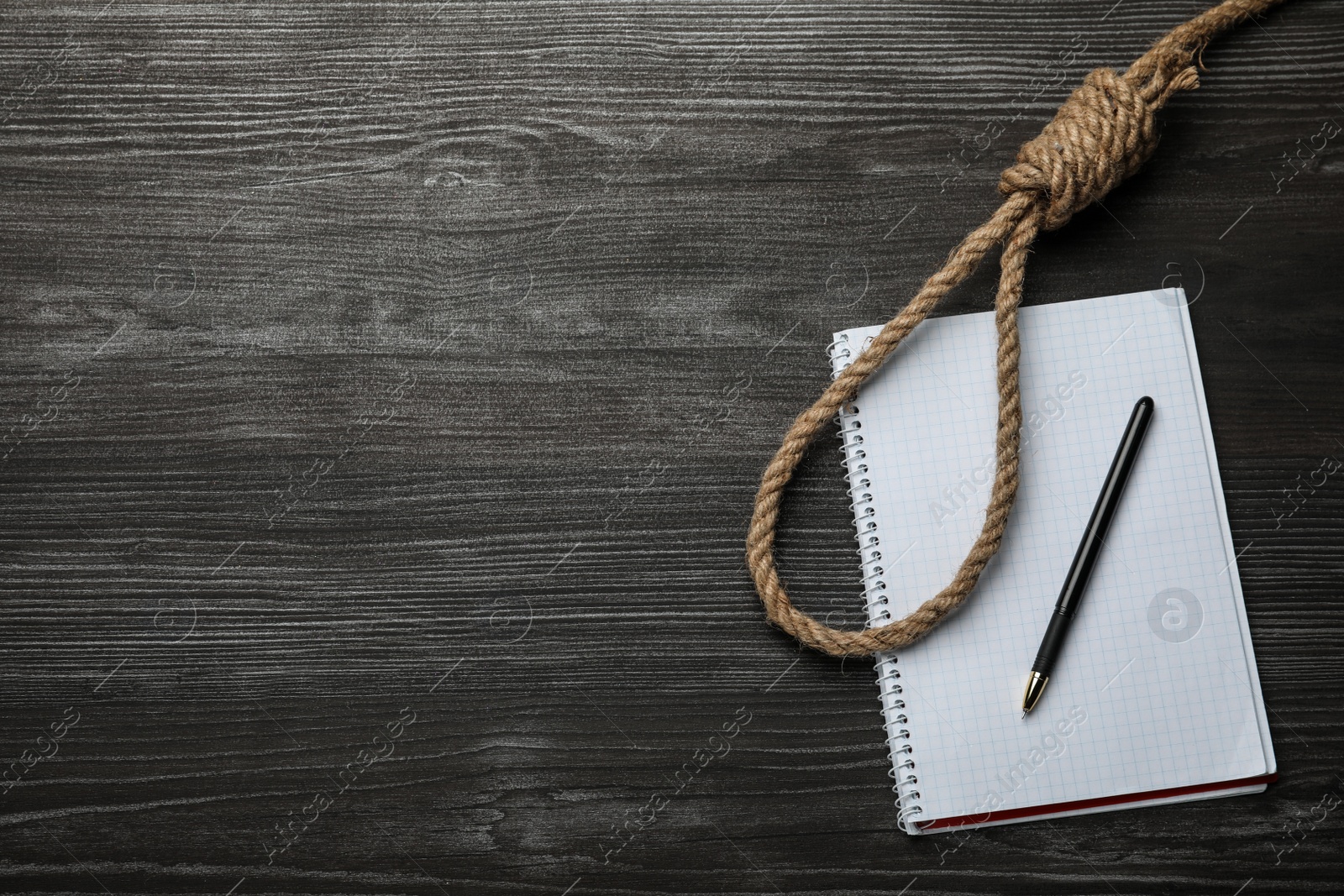 Photo of Rope noose and blank notebook with pen on black wooden table, flat lay. Space for text