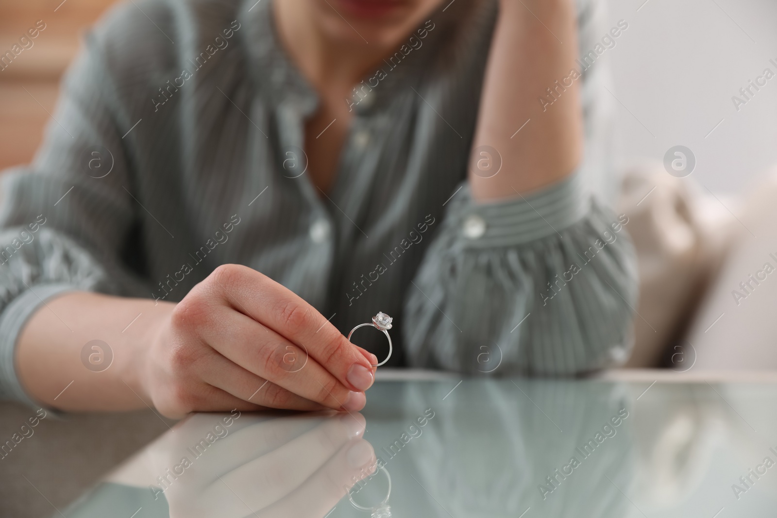 Photo of Woman holding wedding ring at table indoors, closeup. Divorce concept