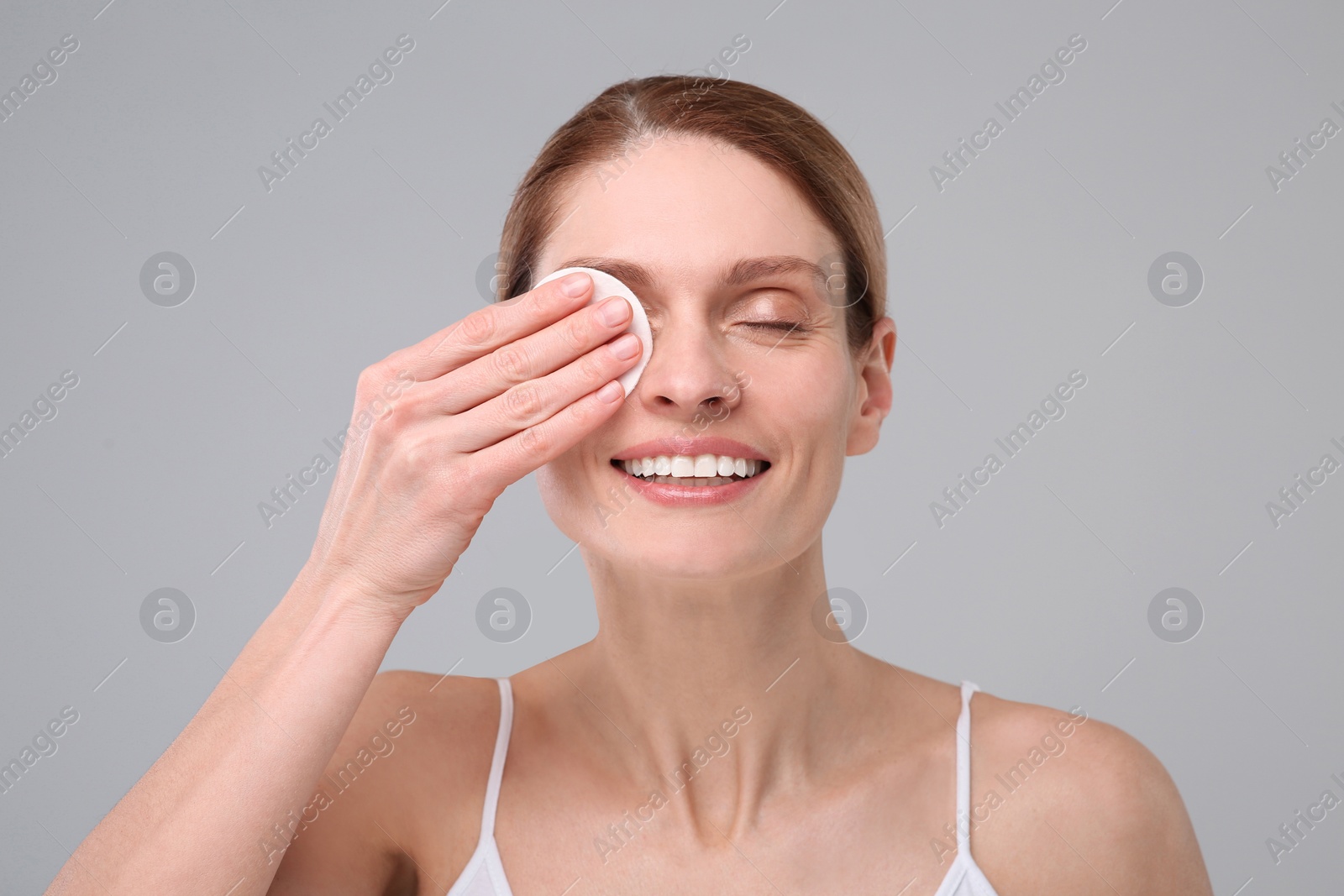 Photo of Beautiful woman removing makeup with cotton pad on gray background