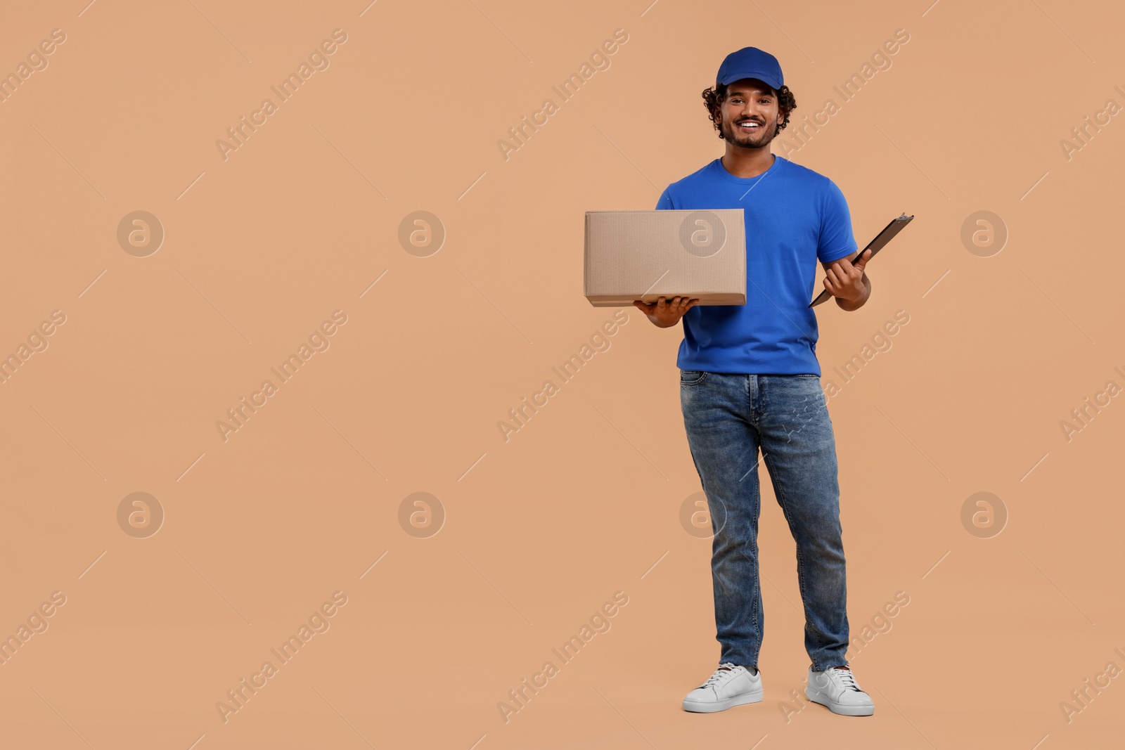 Photo of Happy courier with parcel and clipboard on light brown background, space for text