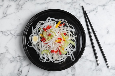 Photo of Plate of tasty noodles and chopsticks on marble table, flat lay