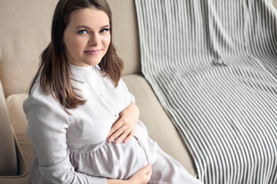 Beautiful pregnant woman sitting on sofa at home