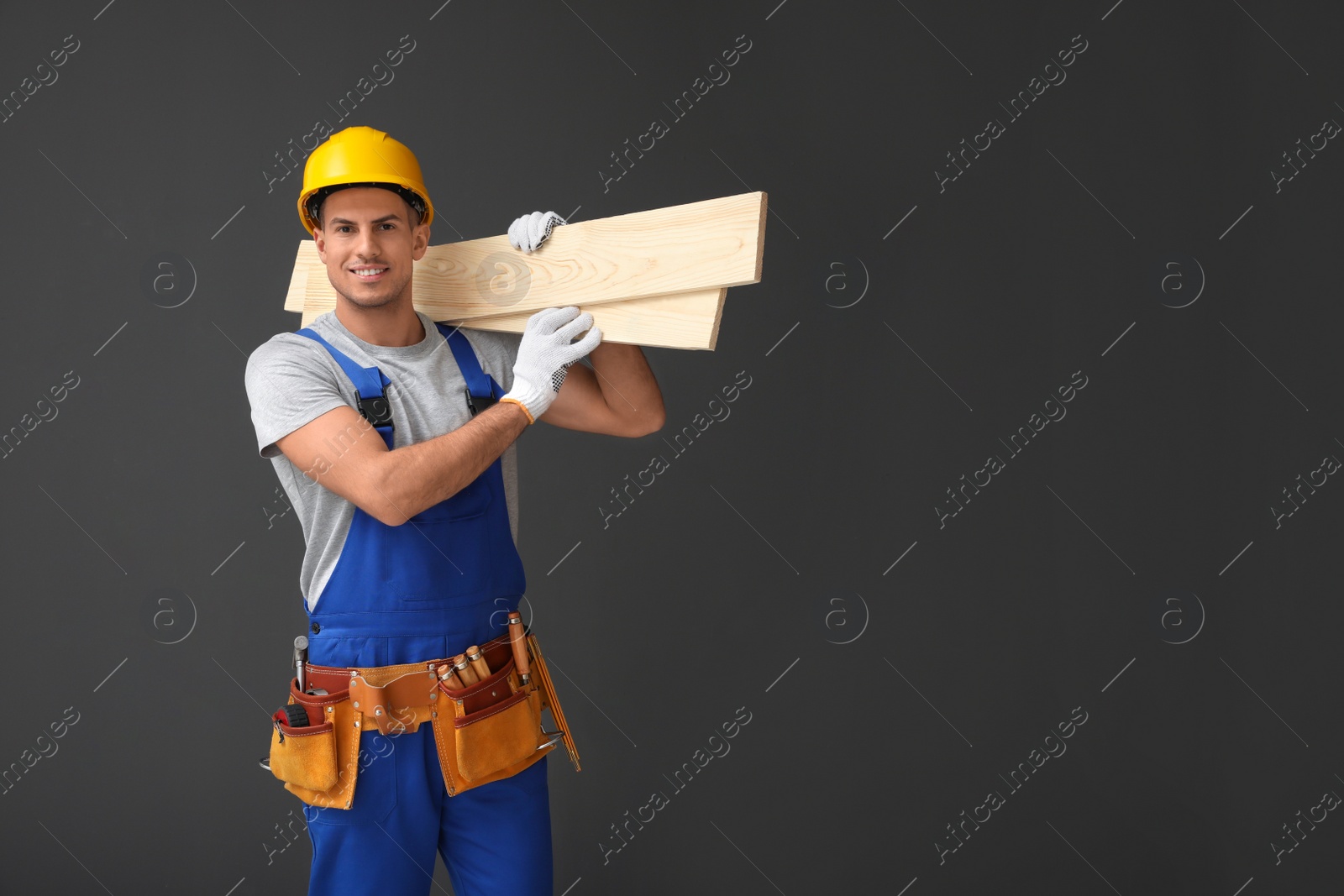 Photo of Handsome carpenter with wooden planks on dark background. Space for text