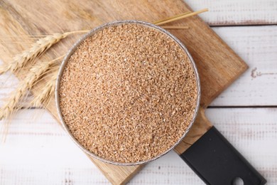 Dry wheat groats in bowl and spikelets on white wooden table, top view