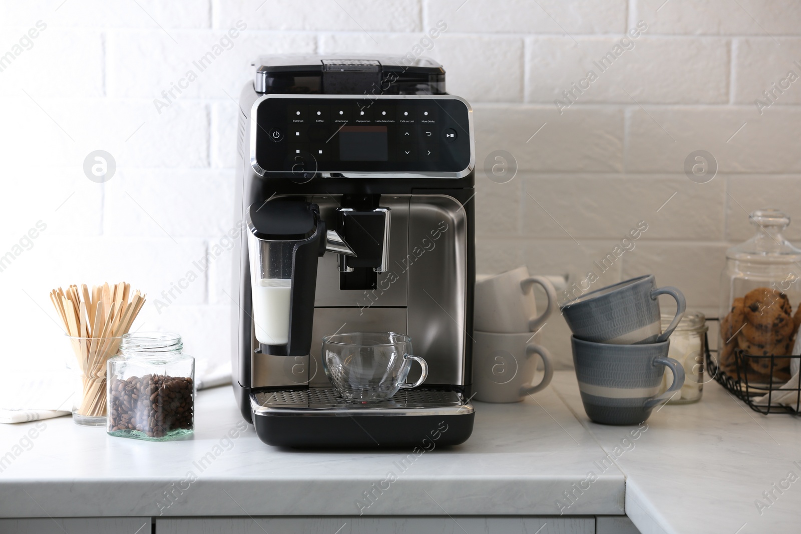 Photo of Modern electric coffee machine with glass cup on white marble countertop in kitchen