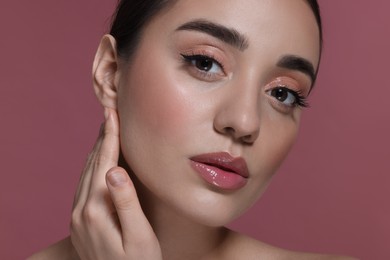 Photo of Portrait of beautiful young woman with perfect makeup on dark pink background, closeup