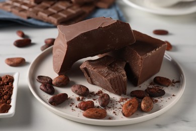 Photo of Pieces of tasty milk chocolate and cocoa beans on white table, closeup