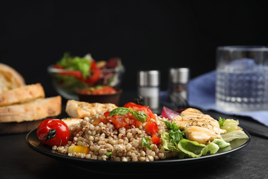 Photo of Tasty buckwheat porridge with meat and vegetables on black table