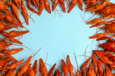 Photo of Frame of delicious boiled crayfishes on light blue background, flat lay. Space for text
