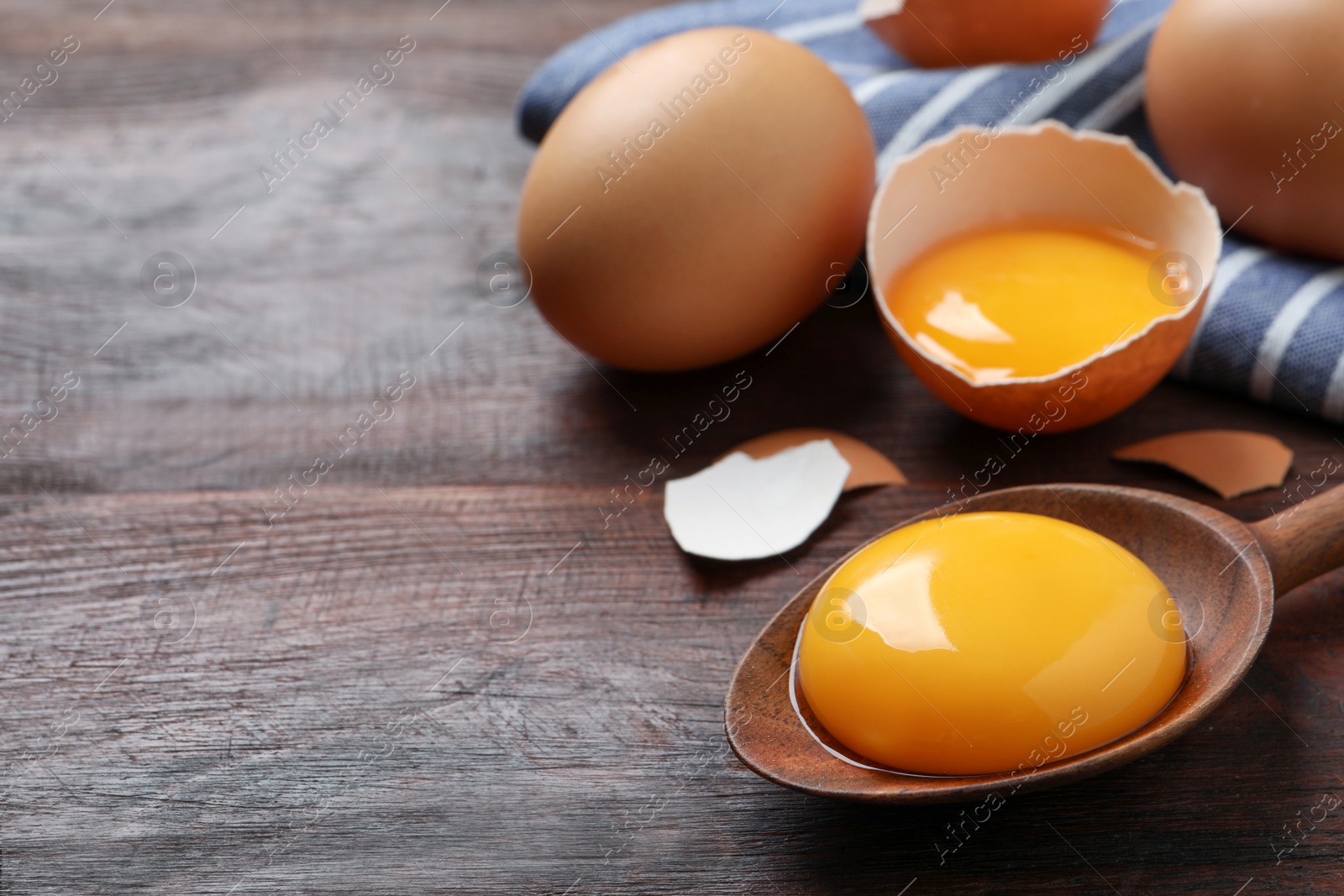 Photo of Spoon with raw egg yolk on wooden table, closeup. Space for text