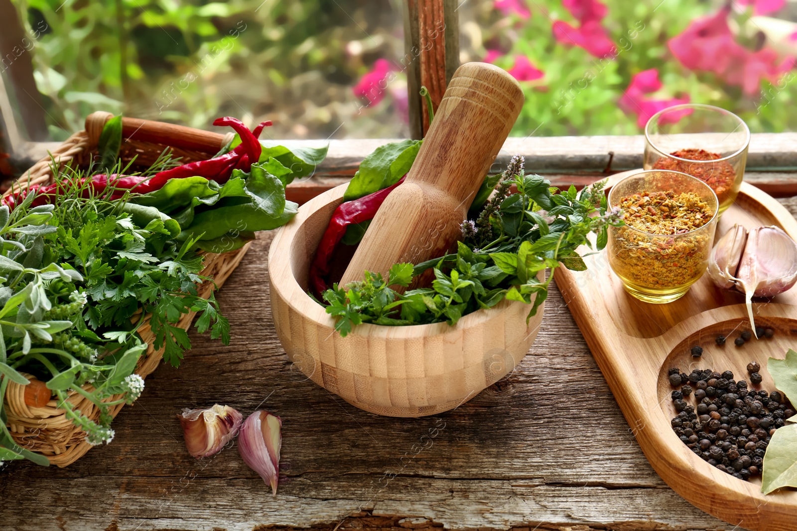 Photo of Mortar with pestle, fresh green herbs and different spices on wooden table near window